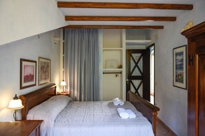 A bedroom with a wooden headboard, a bed with white bedding, two bedside lamps, and a window with curtains. - Casa Ortobene with mountain view (Nuoro)