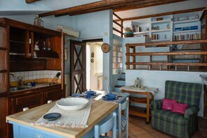 A kitchen with wooden cabinets, a dining table, and a chair. There is a bookshelf with books and decorative items. - Casa Ortobene with mountain view (Nuoro)