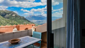 Un balcón con macetas de terracota, una mesa y una silla, con vistas a un paisaje montañoso.