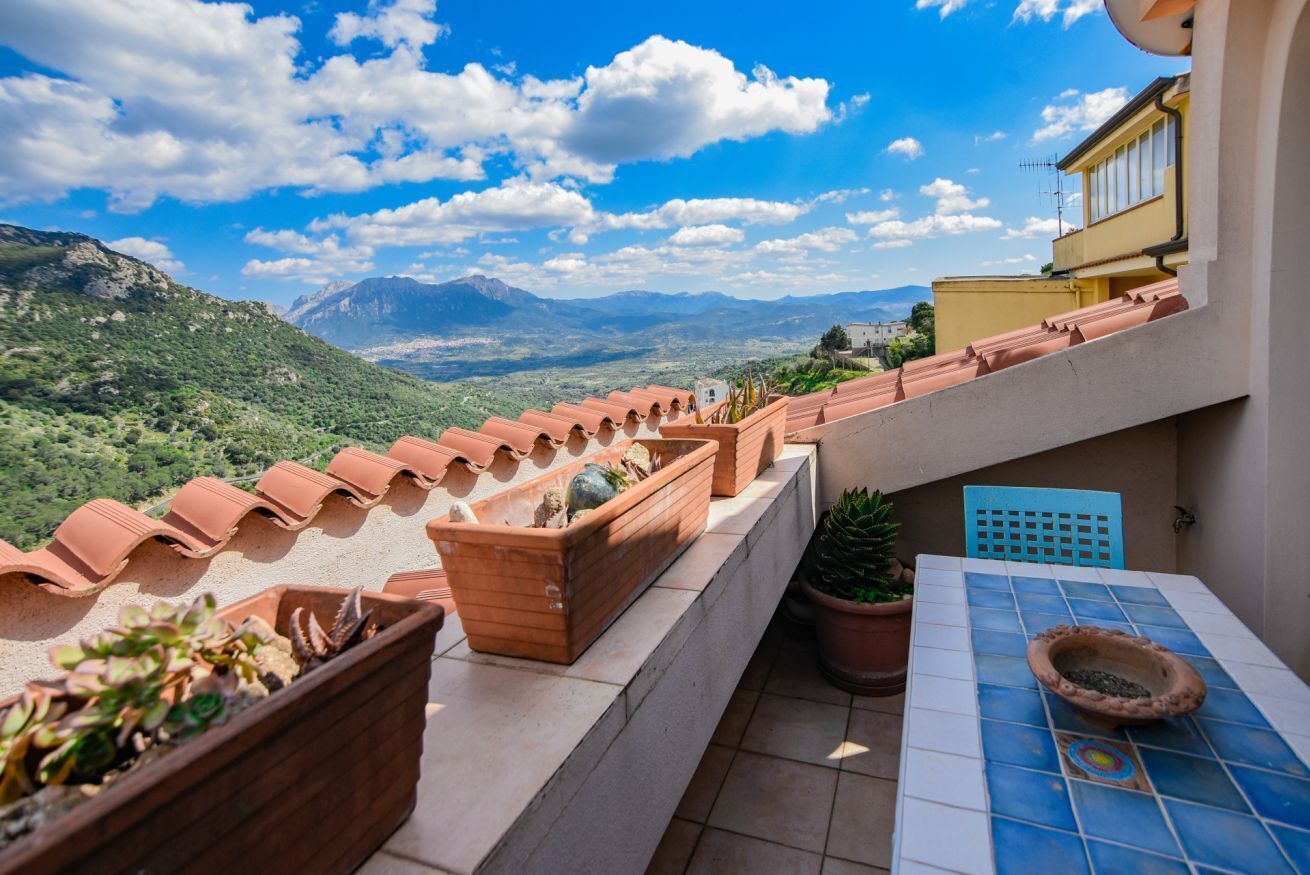 A terrace with terracotta pots, a tiled table, and a view of mountains.