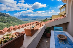 A terrace with terracotta pots, a tiled table, and a view of mountains.