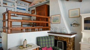 Una habitación con cama elevada, chimenea, sofá y estanterías con diversos objetos.
