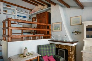 Een kamer met een hoogslaper, een open haard, een bank en planken met diverse spullen.