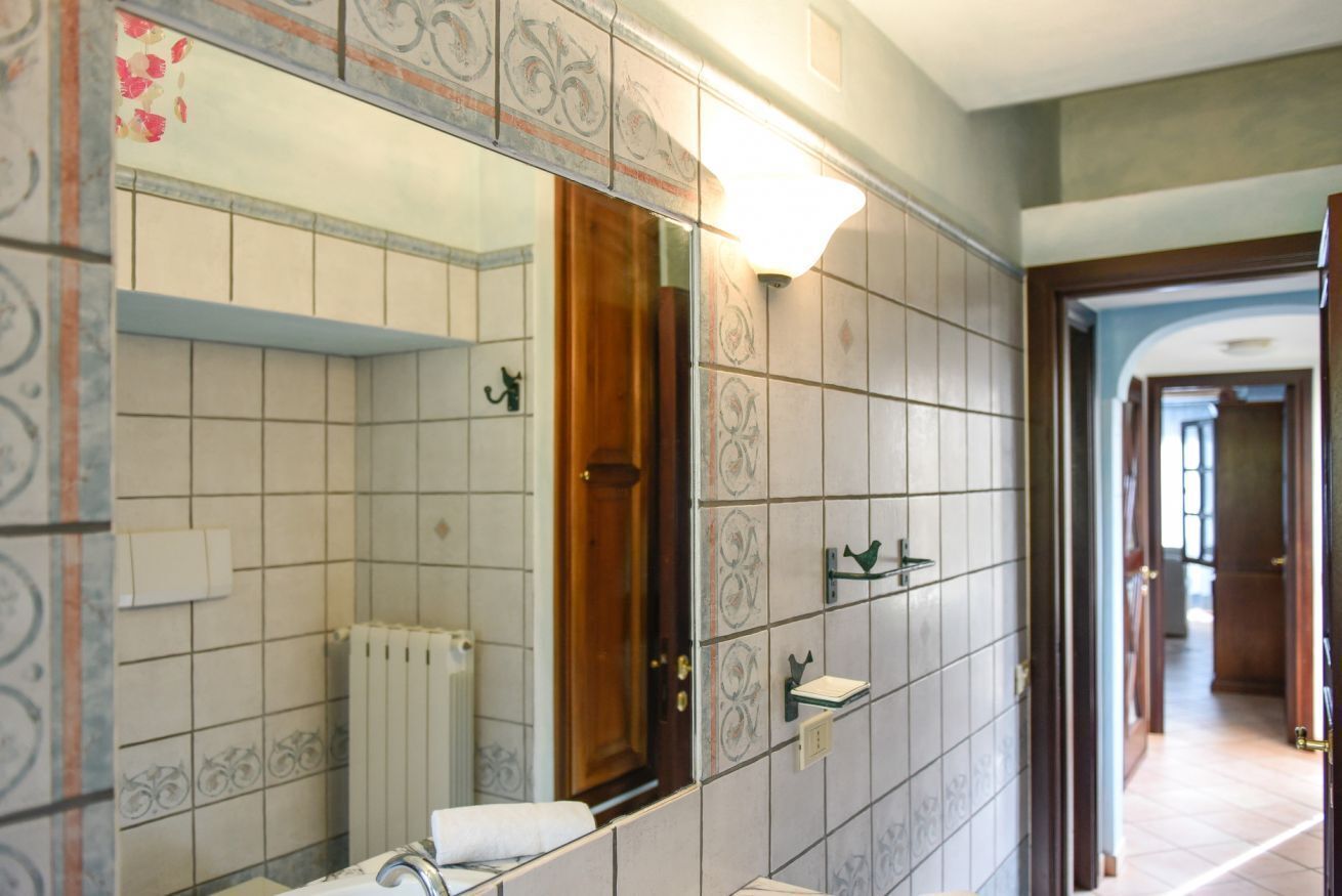 Ein Badezimmer mit großem Spiegel, Fliesenwänden, einem Heizkörper und einer Holztür.