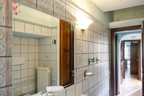 A bathroom with a large mirror, tiled walls, a radiator, and a wooden door. - Casa Ortobene with mountain view (Nuoro)