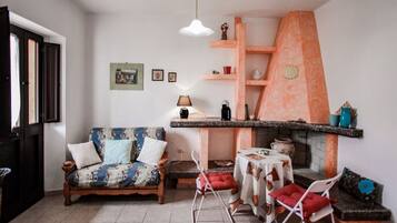 Una sala de estar con un sofá, una mesita, una silla, una chimenea y un estante con objetos decorativos.