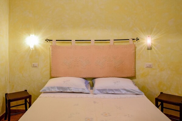 A room with a bed, two nightstands, and wall-mounted lights.