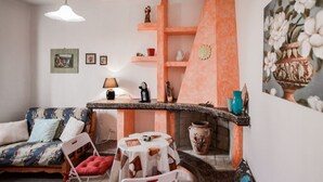 A cozy living room with a sofa, chairs, a small table, and a decorative shelf. - Giardino dei Limoni Rooms 1 (Oliena)