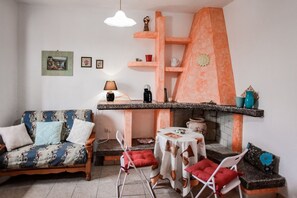 A living room with a sofa, chairs, a table, a fireplace, and shelves with decorative items. - Giardino dei Limoni Rooms 2 (Oliena)
