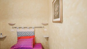 A bedroom with a bed, pillows, a wall-mounted shelf, and a framed picture. - Giardino dei Limoni Rooms 2 (Oliena)