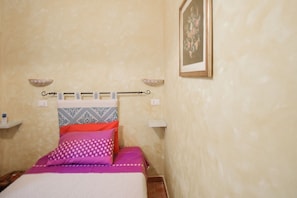 Une chambre à coucher avec un lit, des oreillers, une étagère fixée au mur et un tableau encadré.