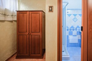 Ein Holzschrank in einer Diele, durch eine offene Tür ist ein gefliestes Badezimmer zu sehen.