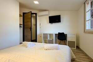 Quarto com cama, escrivaninha, cadeira, televisão e porta aberta.