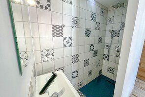 Ein Badezimmer mit einem weißen Waschbecken, einer Dusche und einer gefliesten Wand mit verschiedenen Mustern.