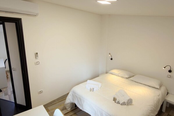 A hotel room with a bed, bedside table, and a mirror.