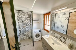 A modern bathroom with a washing machine, a large mirror, and patterned tiles.