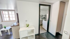 Et moderne hotelværelse med et hvidt skrivebord, en lille plante, et spejl og en dør til et badeværelse.