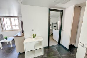Quarto de hotel moderno com escrivaninha branca, uma pequena planta, um espelho e uma porta para o banheiro.