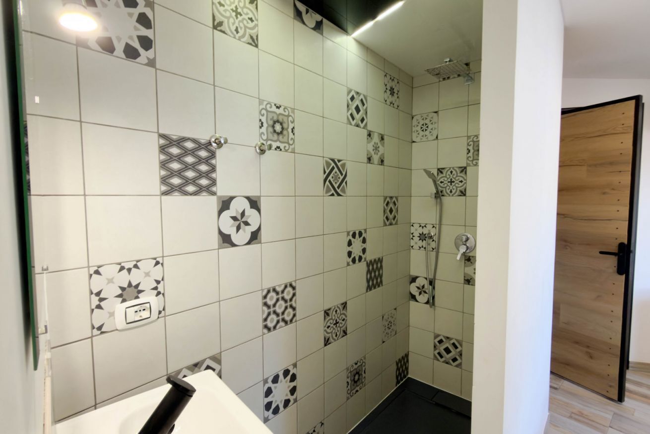 Une salle de bain avec des carreaux décorés, un lavabo blanc et une porte en bois.