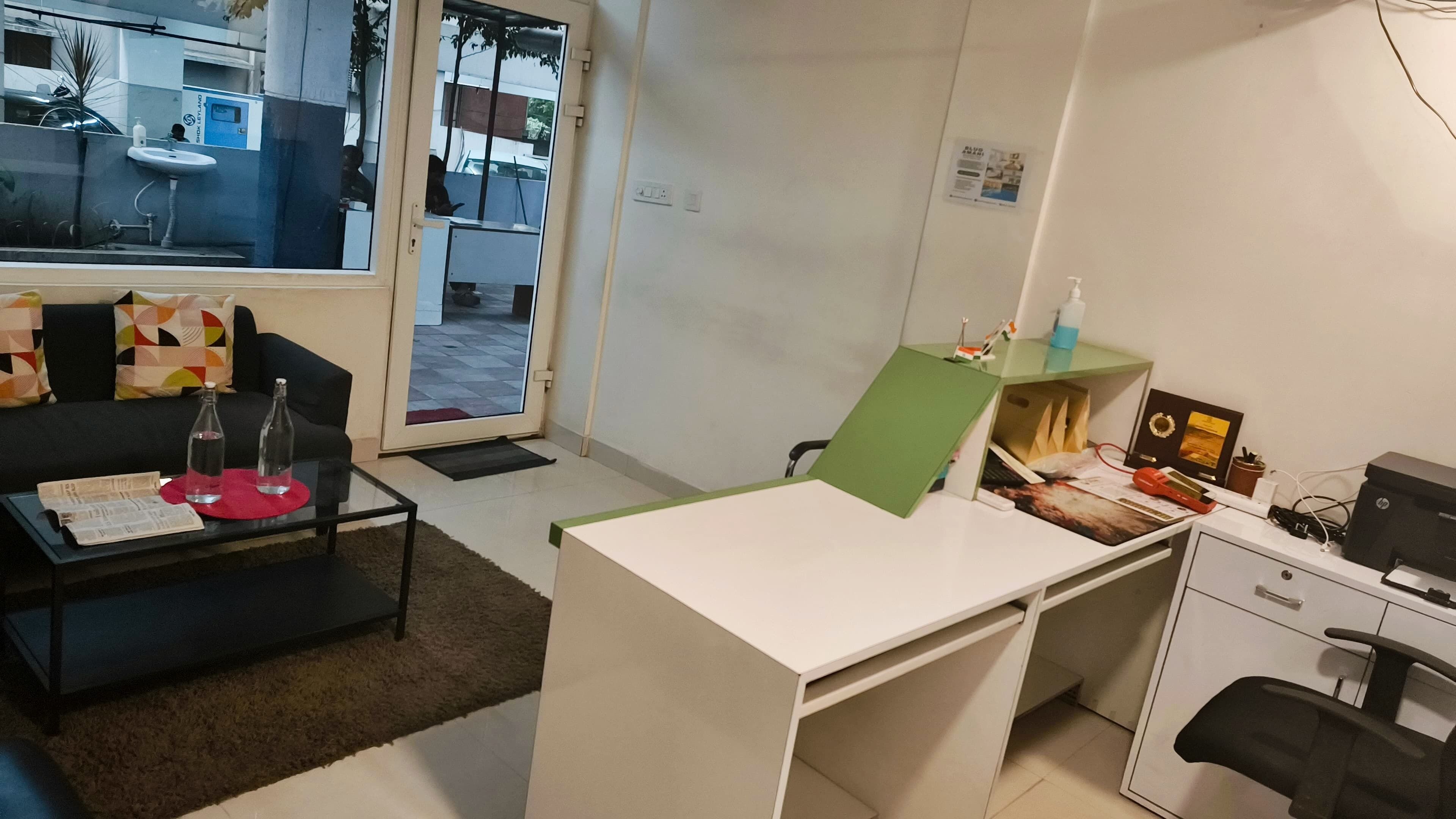 A small office with a desk, chair, and a sofa. There is a window with a view of the outside.