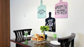 A dining table with a plate of pastries, a green vase, and a glass of green drink. There are two chairs and a wall with three kitchen-themed signs.