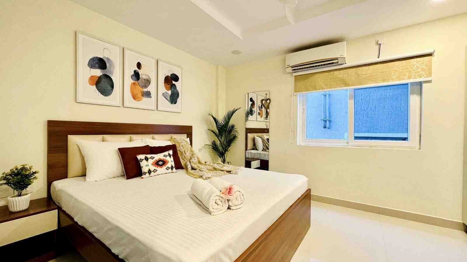 Una camera da letto ordinata con un letto, un comodino con una pianta, una finestra con persiane e un'opera d'arte appesa al muro.