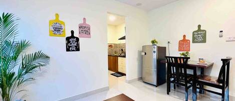 A modern kitchen with a refrigerator, a dining area with a table and chairs, and a potted plant.