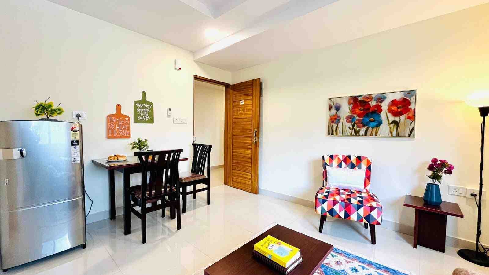 A modern living room with a dining area, a refrigerator, a wooden door, and a colorful chair.