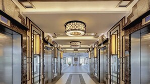 A corridor with a central walkway, flanked by elevators and glass doors, leading to a spacious area with a patterned ceiling and recessed lighting. - 1BR Gem in MNL w/Pool, Fast WiFi, Netflix Near Luneta US Embassy & Intramuros (Manila)
