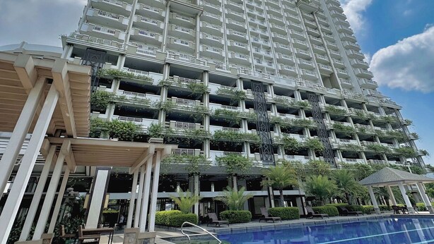 A high-rise building with multiple balconies, a swimming pool, and a covered seating area. - 1BR Gem in MNL w/Pool, Fast WiFi, Netflix Near Luneta US Embassy & Intramuros (Manila)