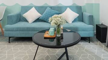 A modern living room with a teal sofa, a round black coffee table, and a geometric patterned rug.