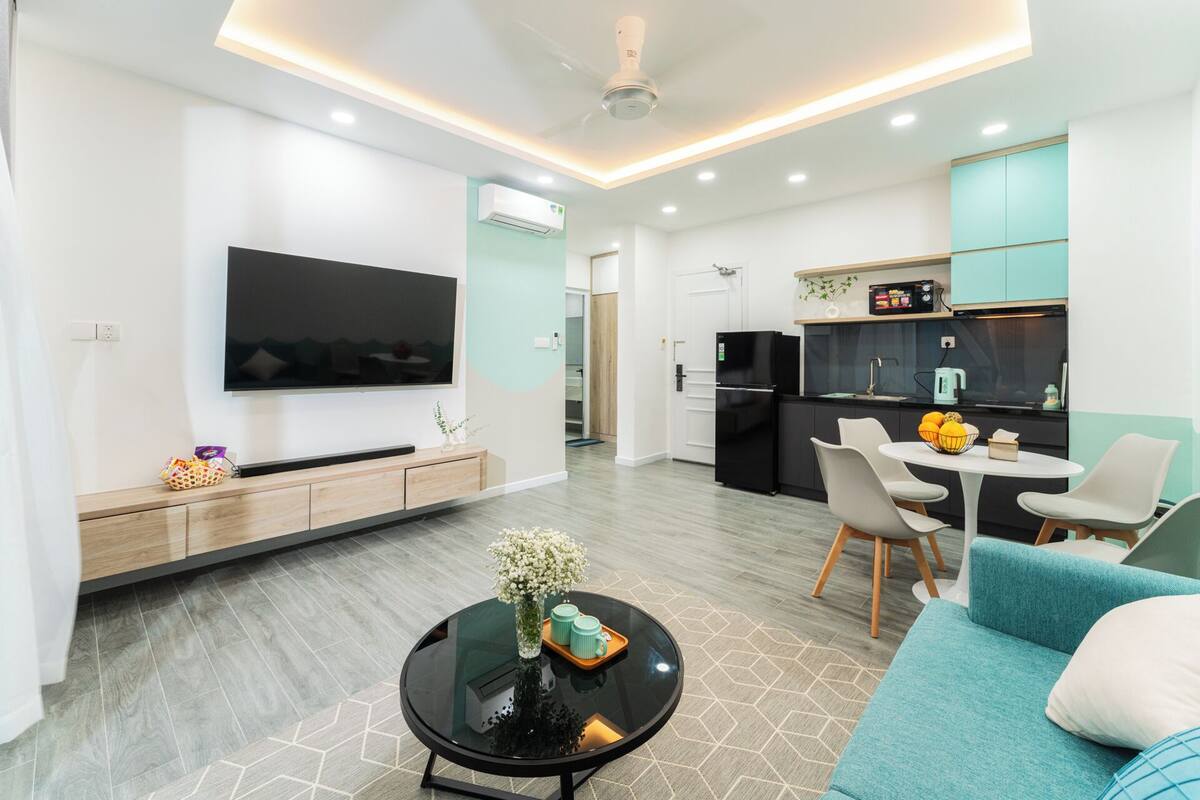 A modern living room with a flat-screen TV, a coffee table with a vase, and a teal sofa.
