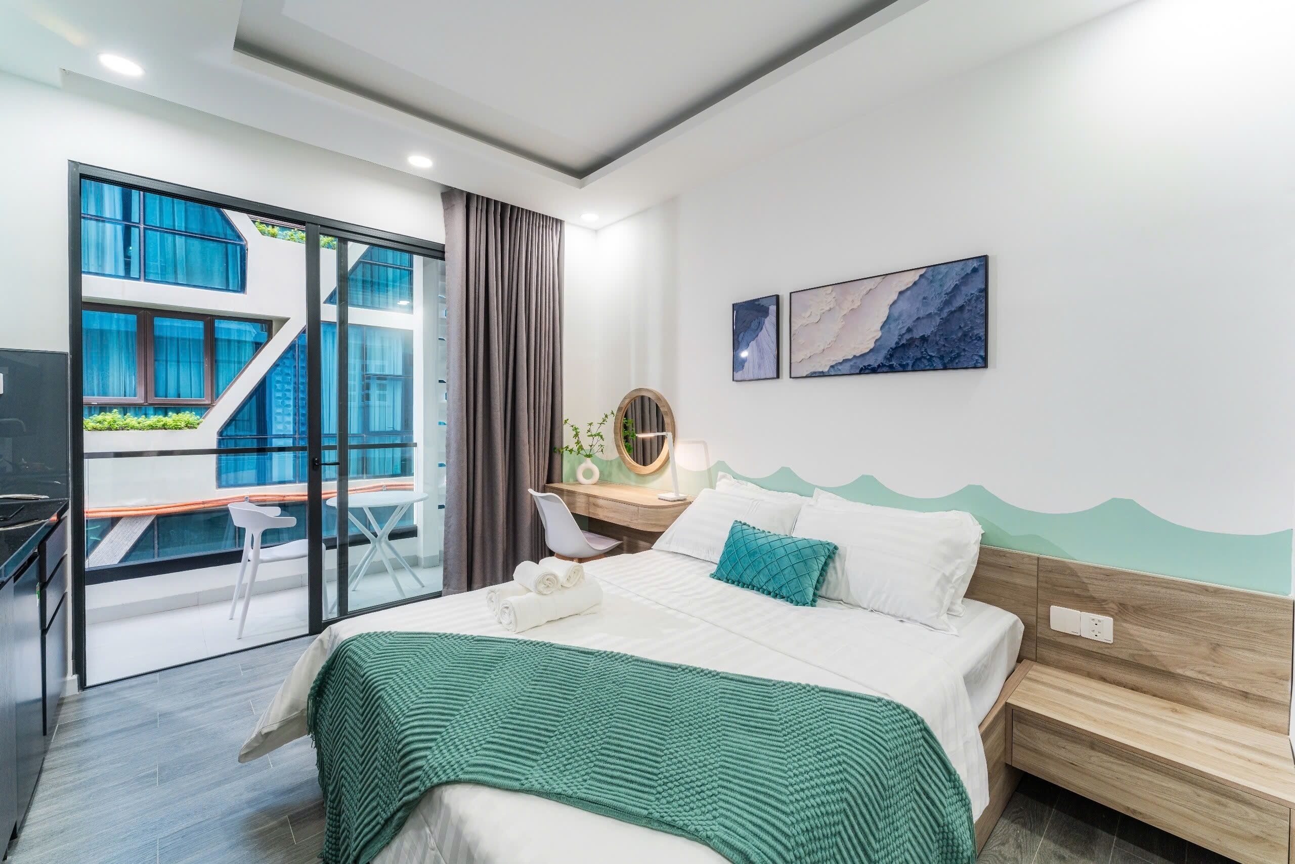 A modern hotel room with a bed, a desk, a chair, and a balcony with a view of the building's exterior.