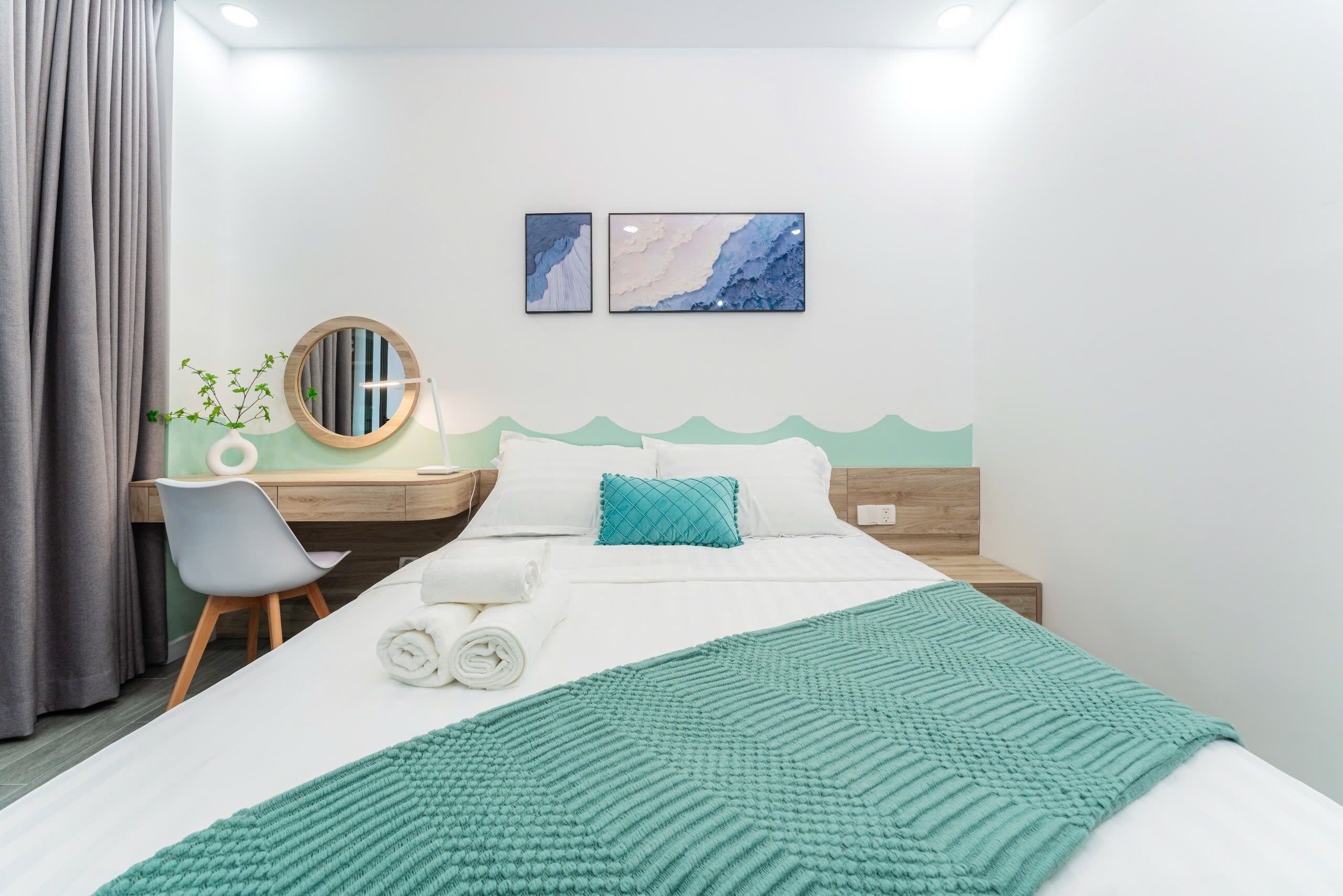Une chambre d’hôtel comprenant un lit, un bureau avec une chaise, un miroir rond et deux œuvres d’art accrochées au mur.