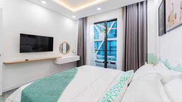 A modern hotel room with a bed, a mounted TV, a bedside table, a window with curtains, and a view of the outside.