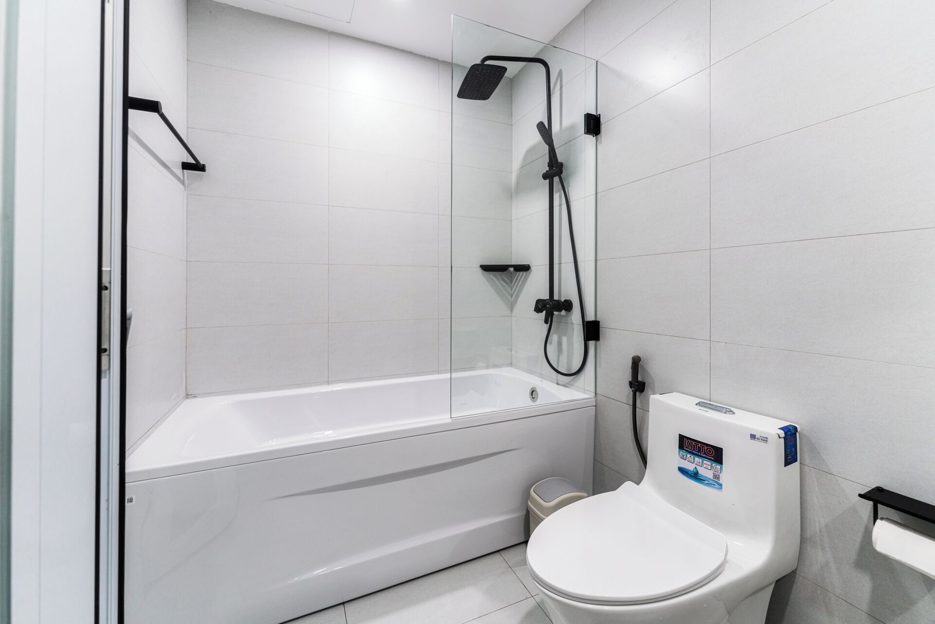 A modern bathroom with a white bathtub, a toilet, and a shower unit.