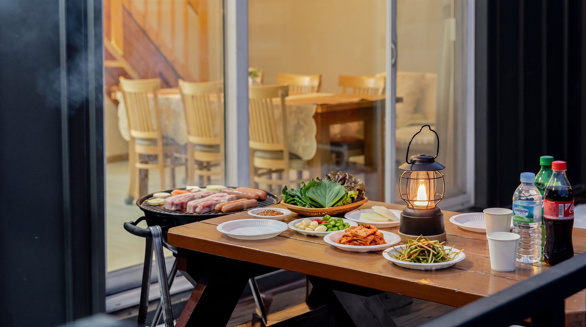 Una mesa dispuesta para una comida con varios platos, una parrilla portátil y un farol.