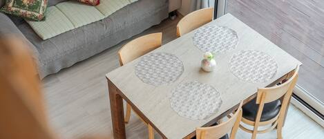 A dining area with a table and chairs, a sofa with cushions, and a window with curtains.
