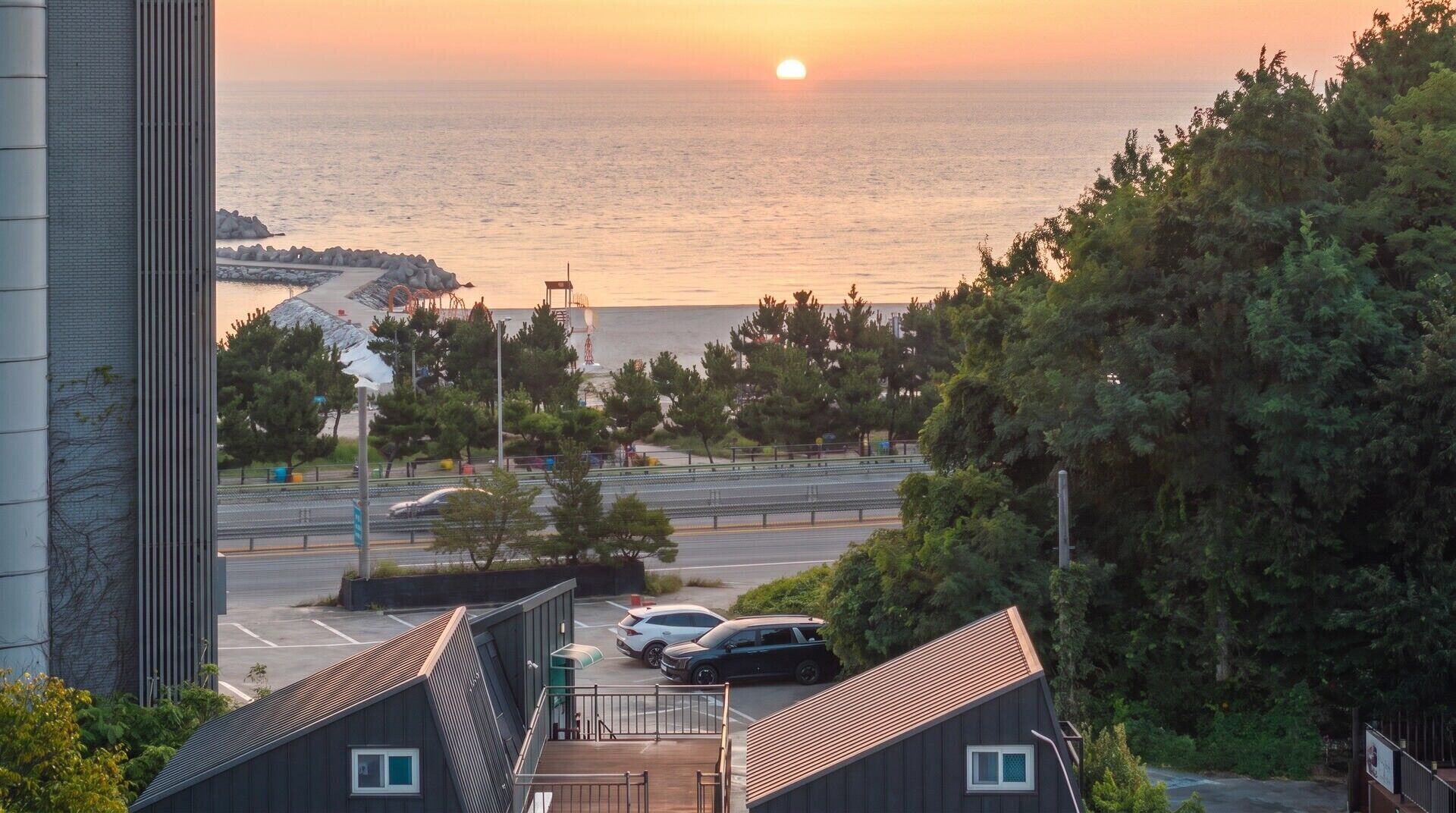 A coastal view with a sunset, a parking area, and a building with a sloped roof.