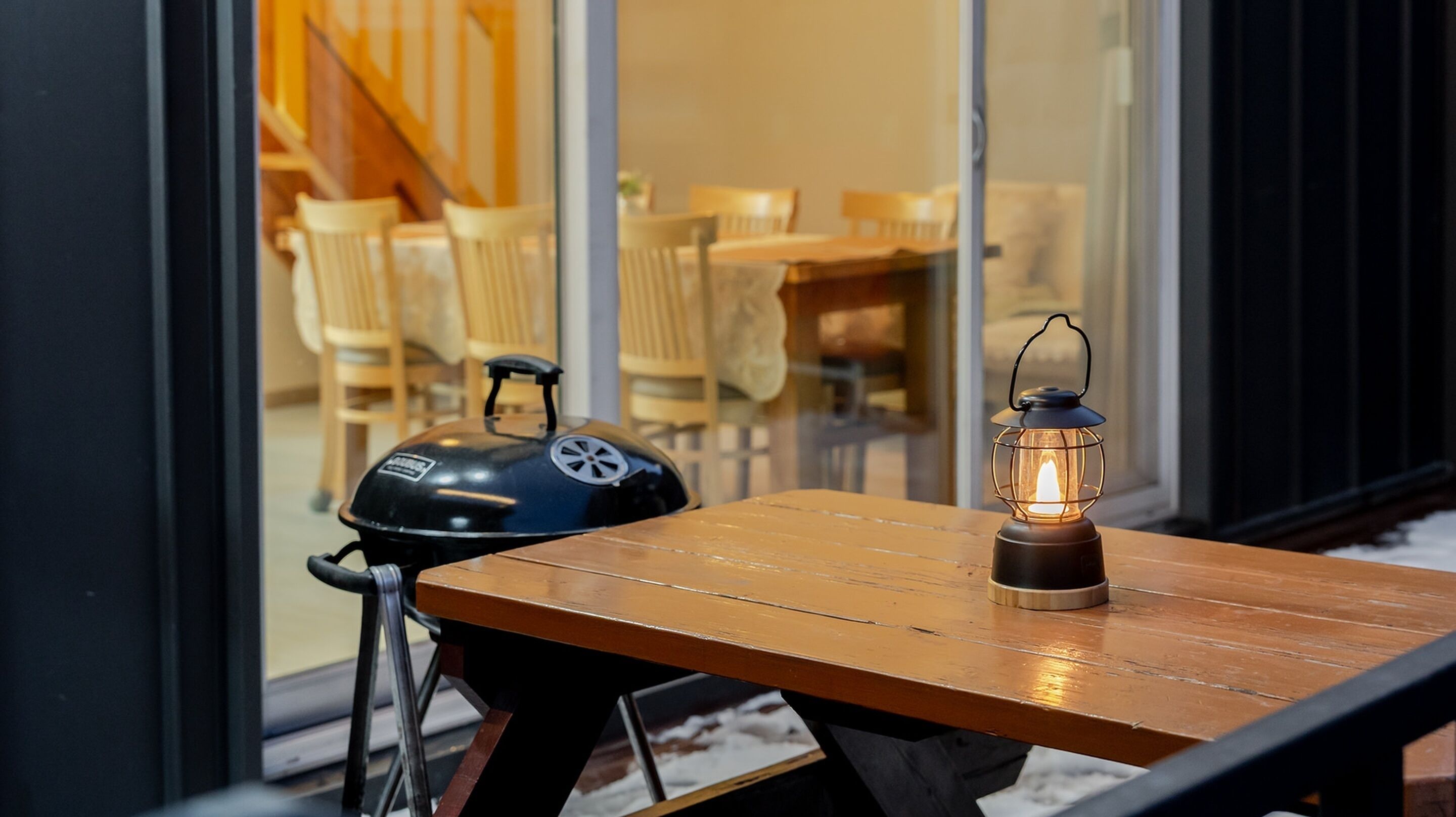 A wooden table with a charcoal grill and a lantern.