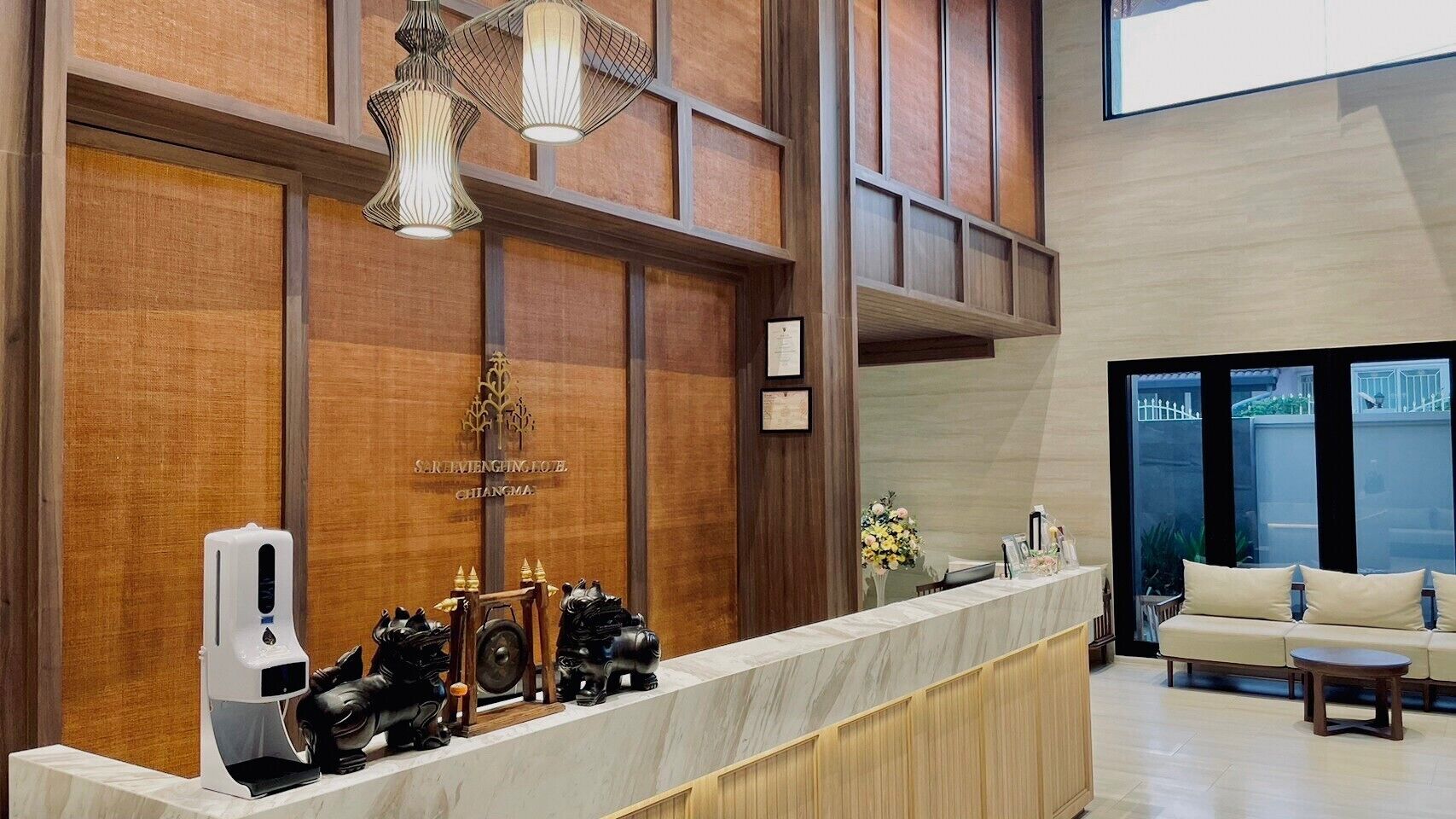 A hotel reception area with a wooden reception desk, a coffee machine, and a sofa in the background.