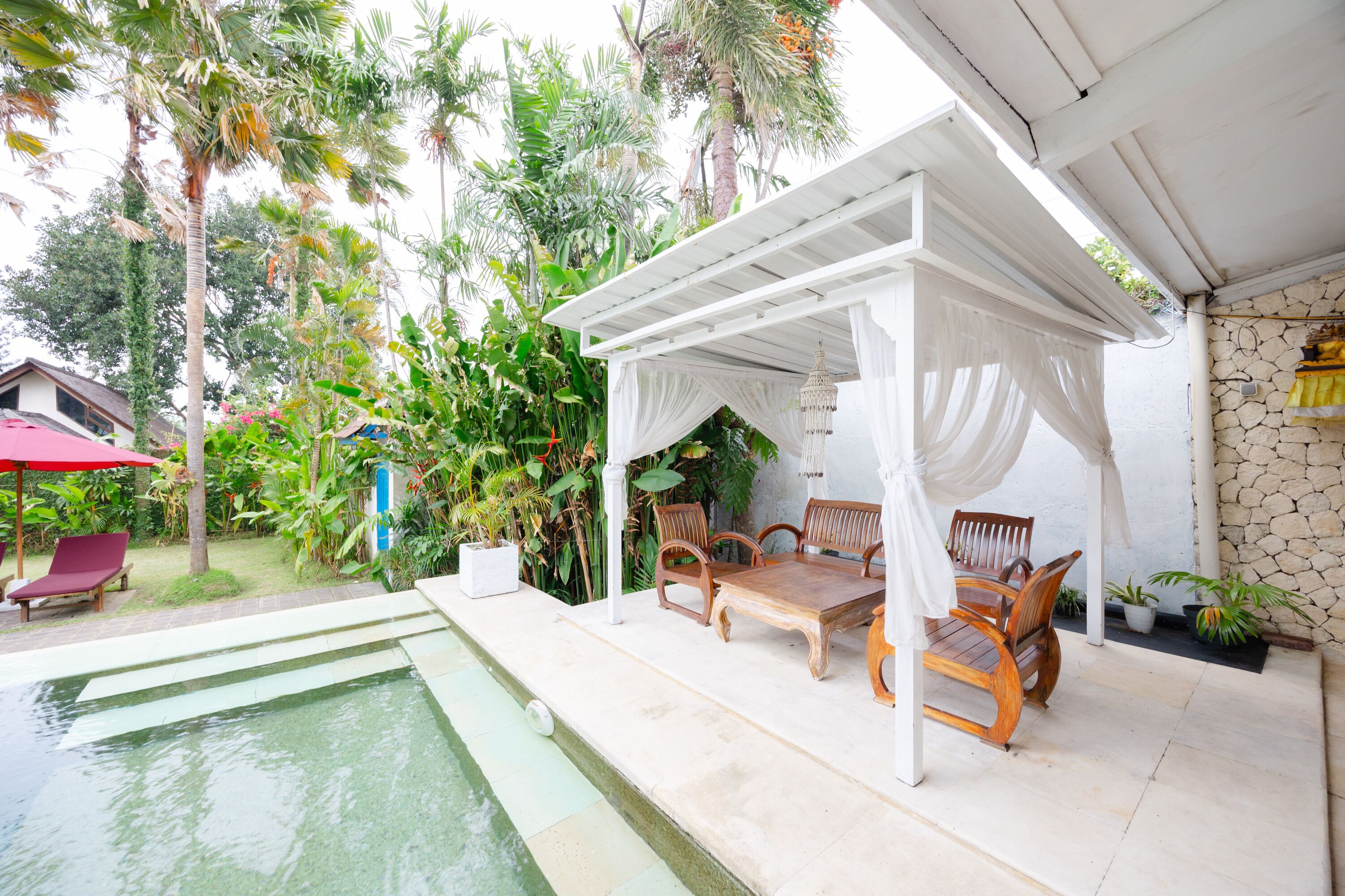 Uma área de estar coberta ao ar livre, com mobiliário de madeira e uma piscina.