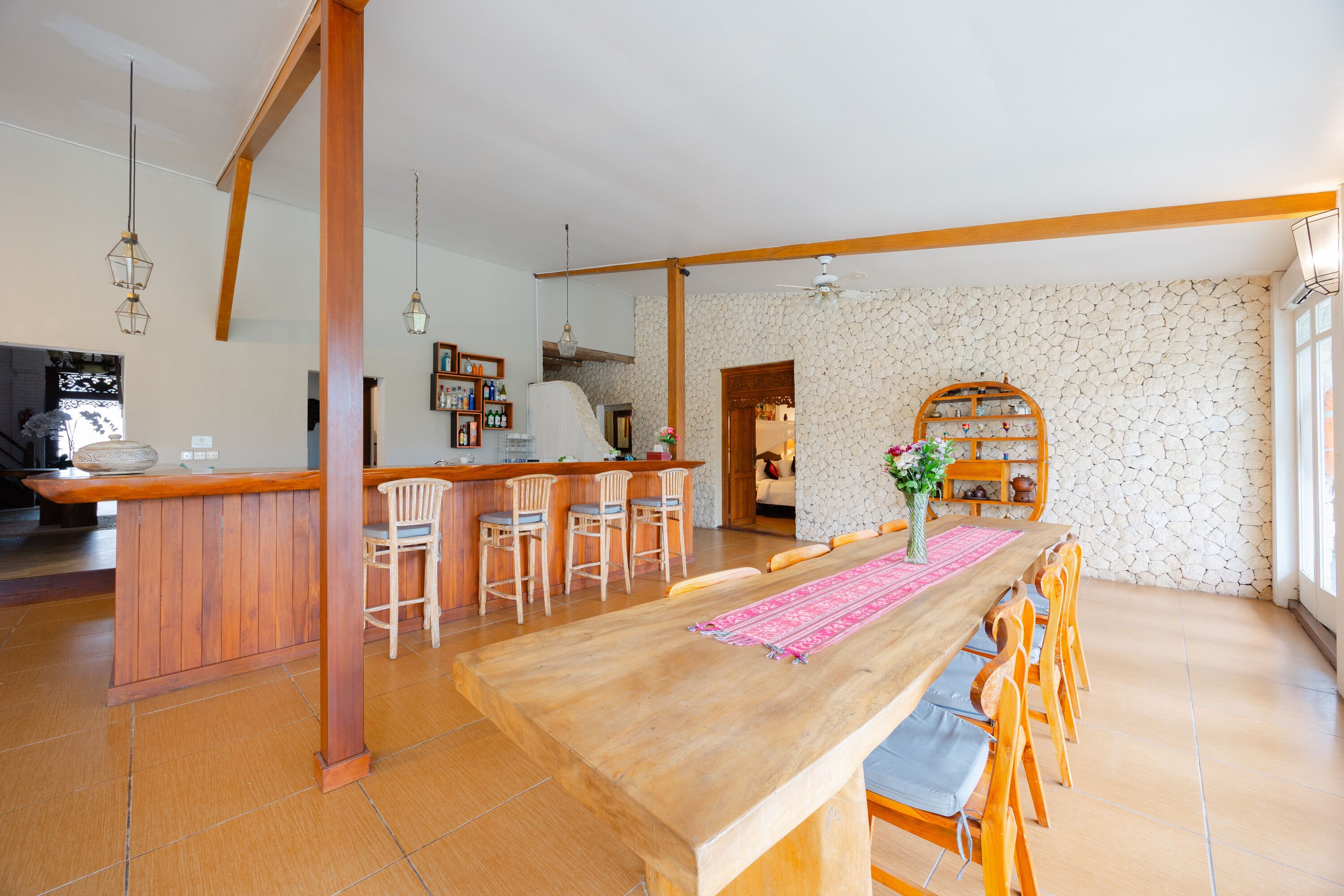 Une cuisine spacieuse dotée d’un îlot central en bois, d’un coin bar avec des tabourets, et d’un espace repas comprenant une longue table et des chaises.