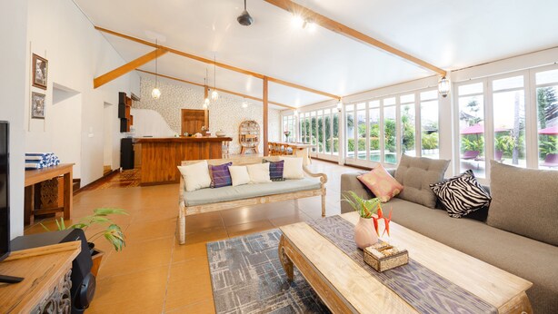 Un vaste espace de vie doté d’un plafond en bois, d’un ensemble de canapés, d’une table basse et d’un coin repas avec une table et des chaises.