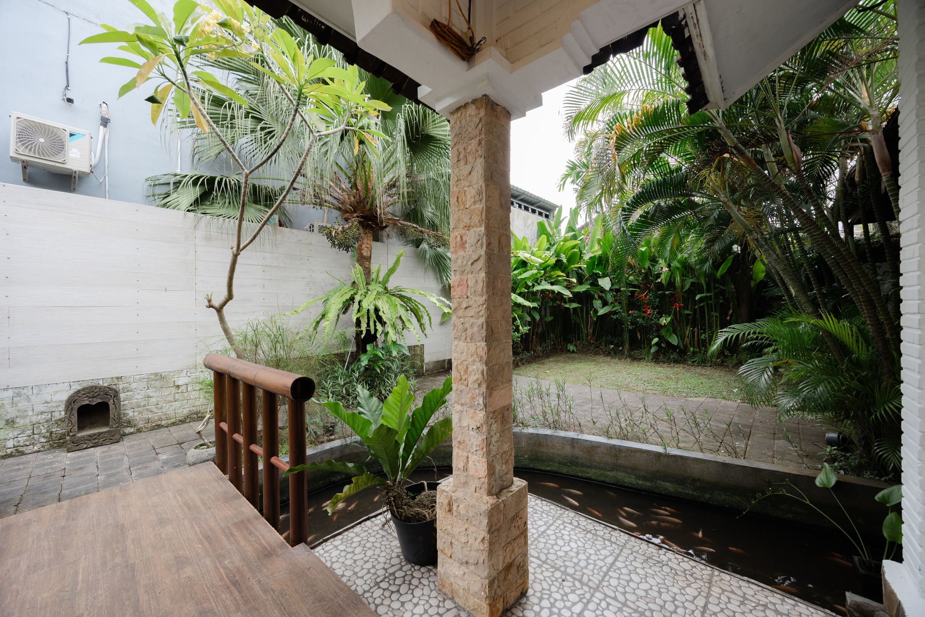 A courtyard with a stone bench, a small water feature, and lush tropical plants.