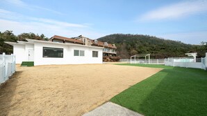 A modern building with a large open area, a fenced sports field, and a hillside in the background. - Gyeongju Purspet Dog Pension (Gyeongju)
