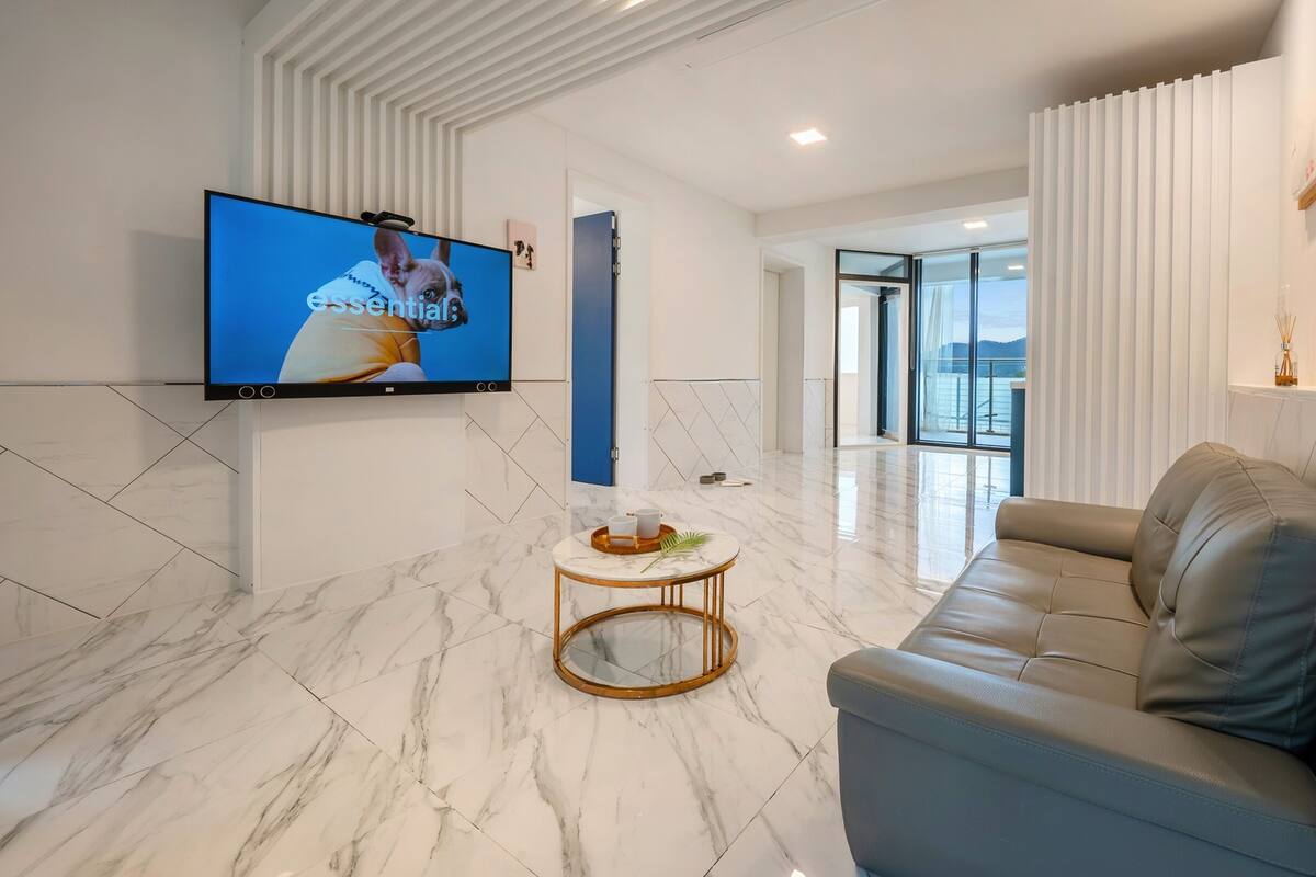 Un soggiorno moderno con un divano in pelle, una televisione montata a parete e un pavimento in marmo.