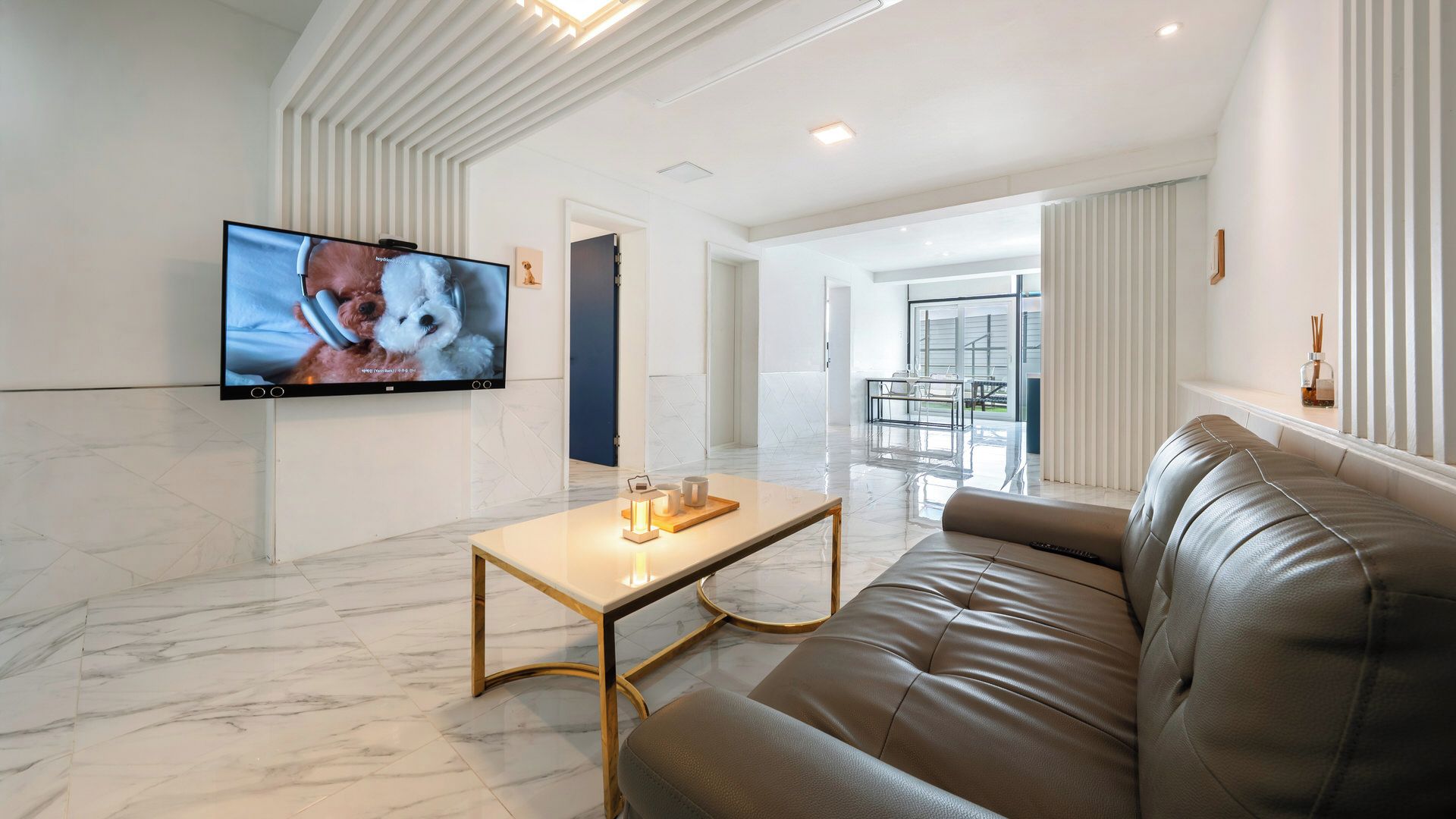 Un salon moderne avec un canapé en cuir, une table basse et un téléviseur à écran plat fixé au mur.