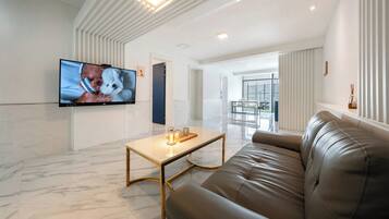 Un salon moderne avec un canapé en cuir, une table basse et un téléviseur à écran plat fixé au mur.