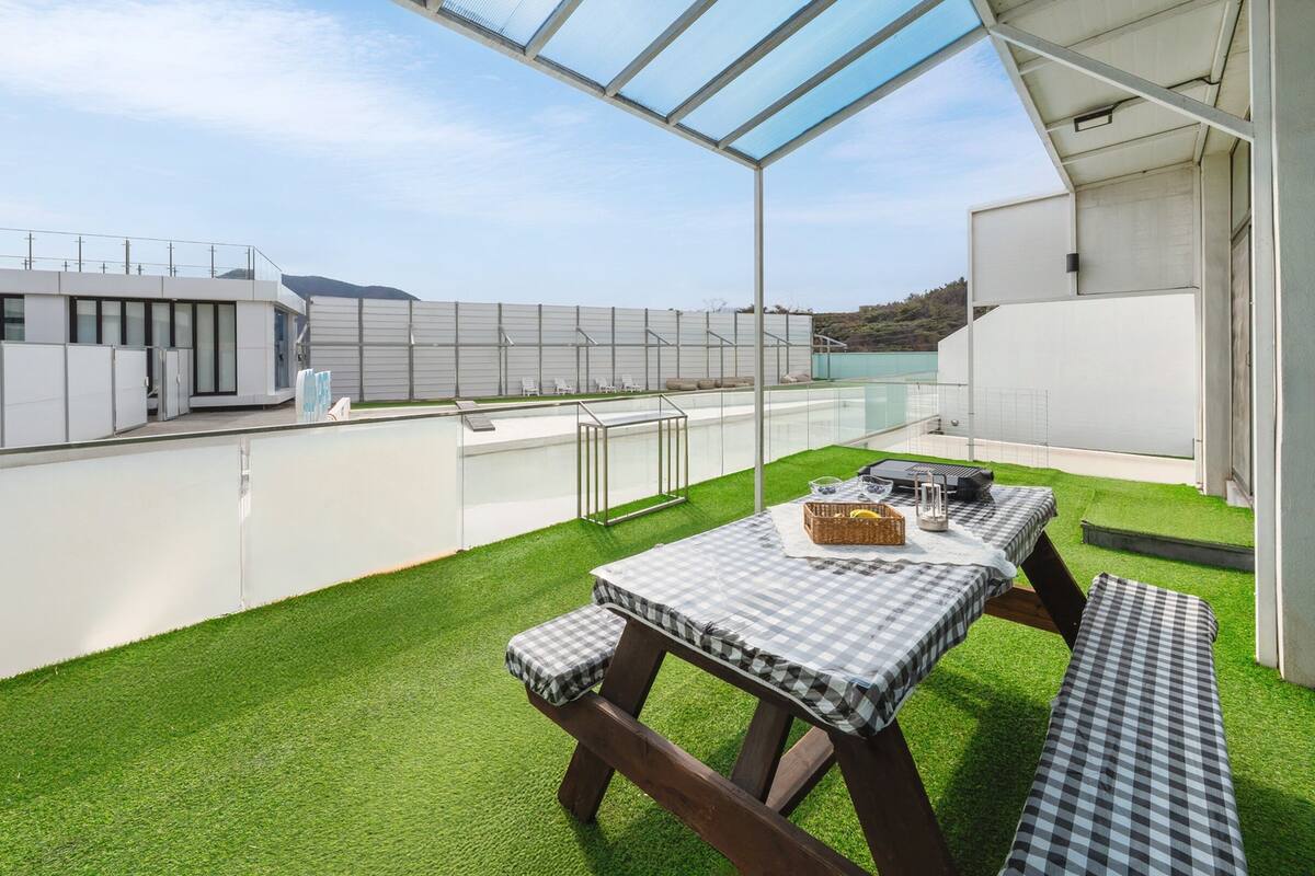 A rooftop terrace with artificial grass, a checkered table, and a grill.